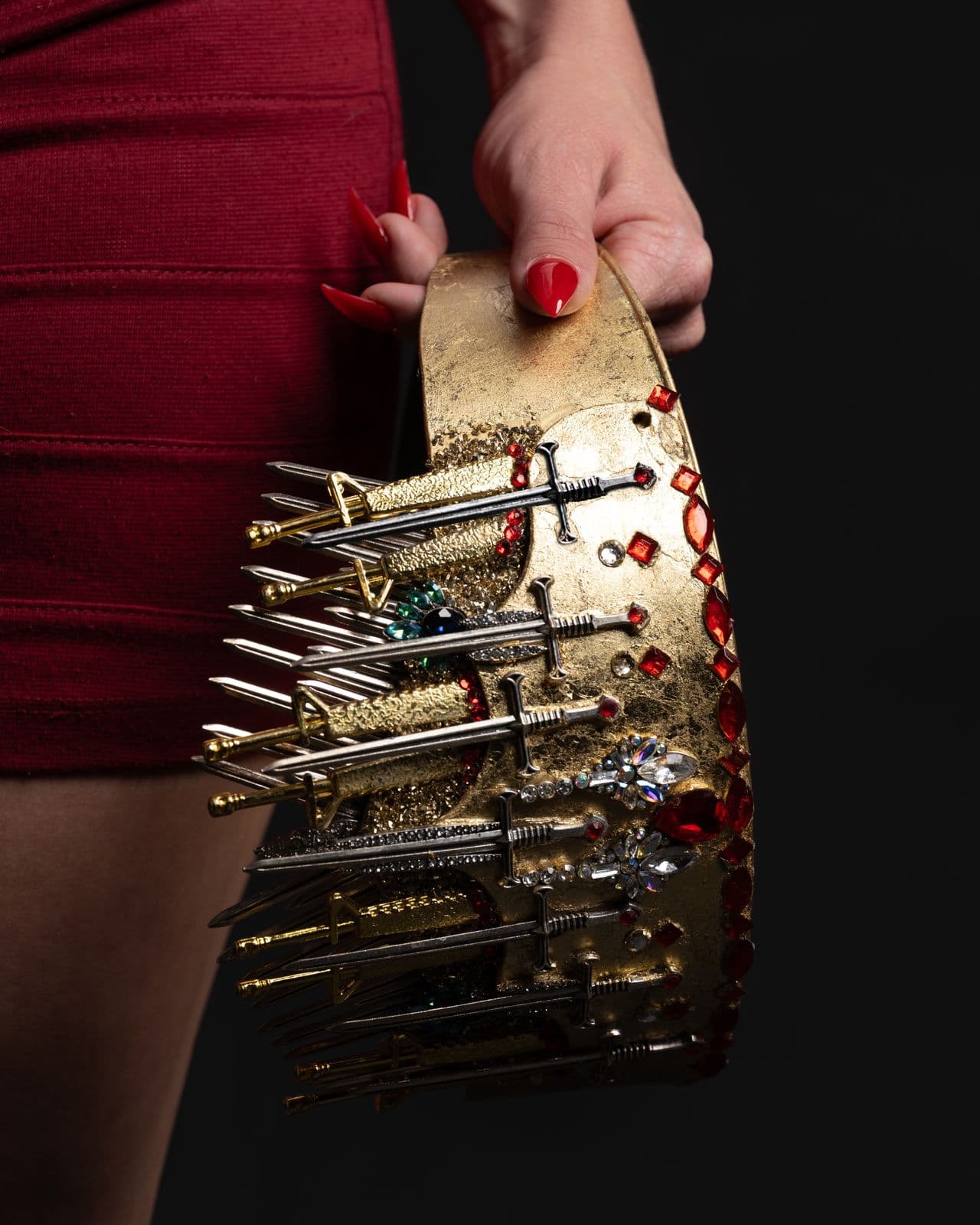 The gold crown held at the hip against a red skirt, its blades catching the light
