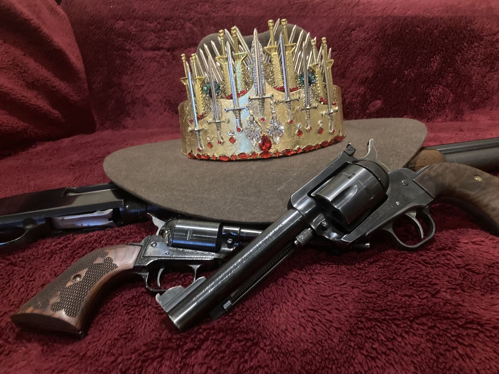 Still life: the gold crown on a cowboy hat, with two revolvers, on red velvet