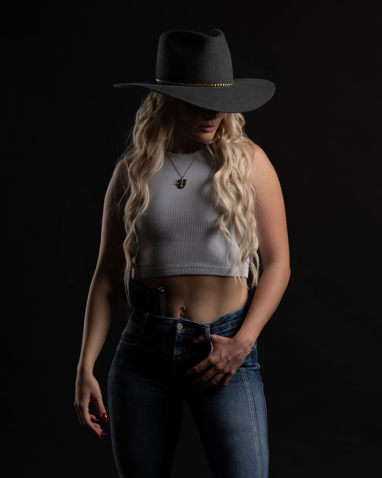 In a white top and jeans under a black cowboy hat, face in shadow, as on the cover